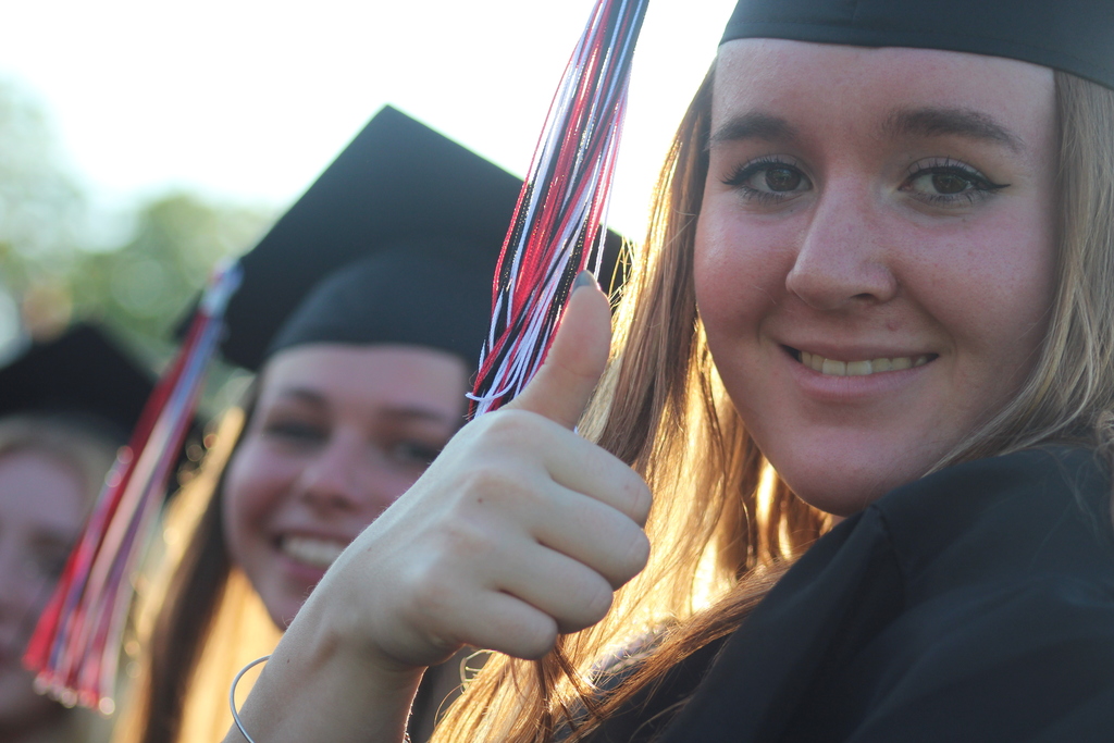 Young woman in graduation cap and gown giving a thumbs up