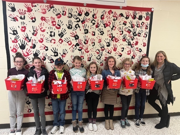 Students holding red gift baskets in front of a banner with black and red handprints