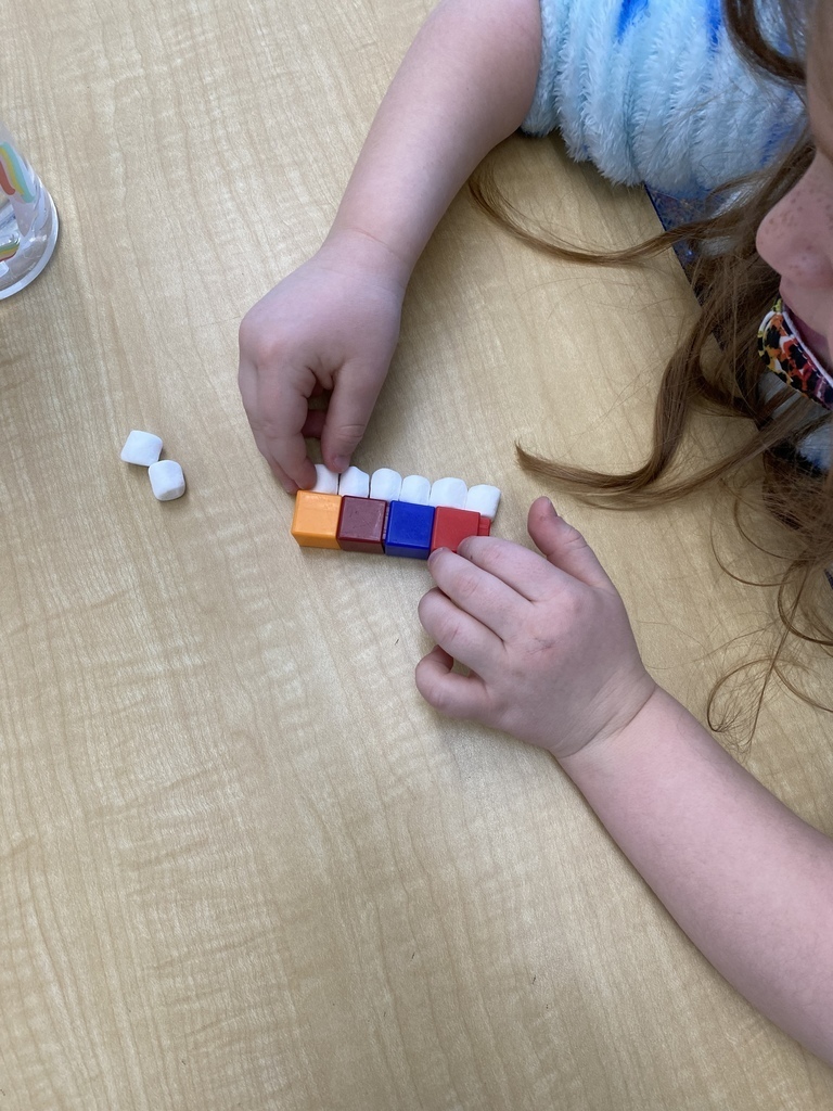 Toddler lining mini marshmallows up with colorful square blocks