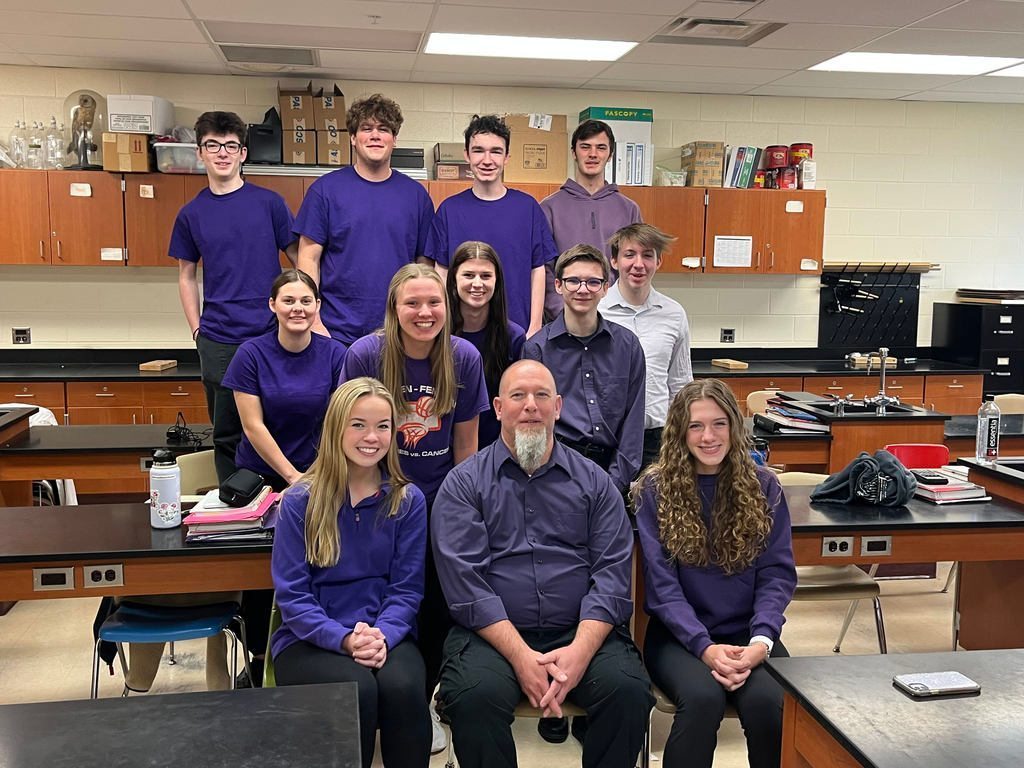Students sitting with a teacher, everyone is wearing a purple shirt