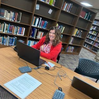 Smiling woman sitting in a library behind a laptop computer