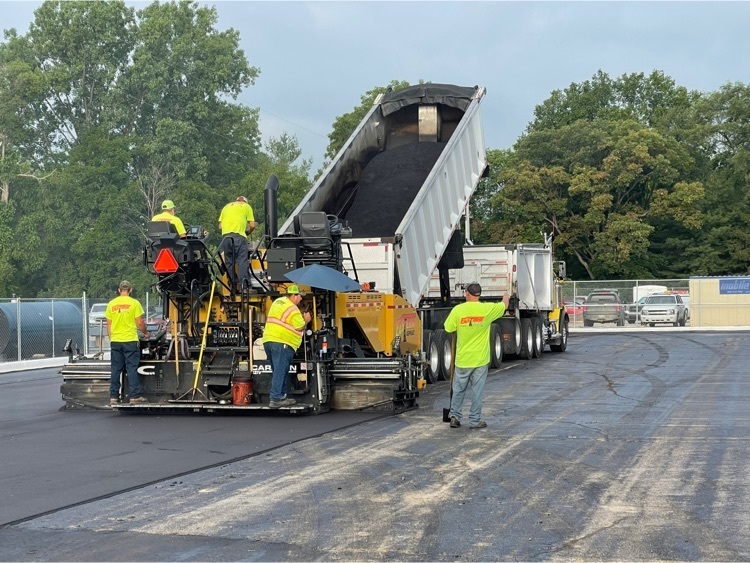 construction crews with trucks putting asphalt surface on student parking lot