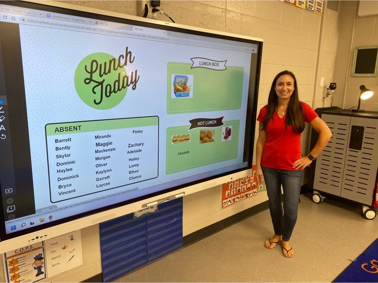teacher in a red shirt standing next to an interactive display board in her classroom