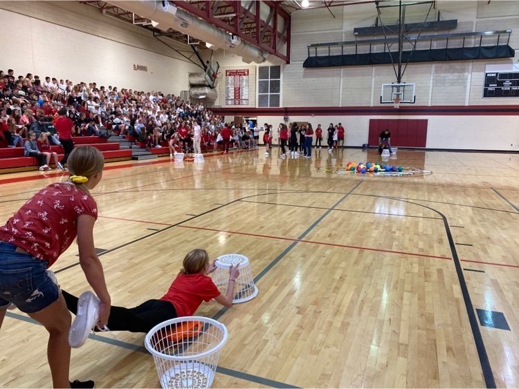 students in bleachers and students on gym floor with a basket 