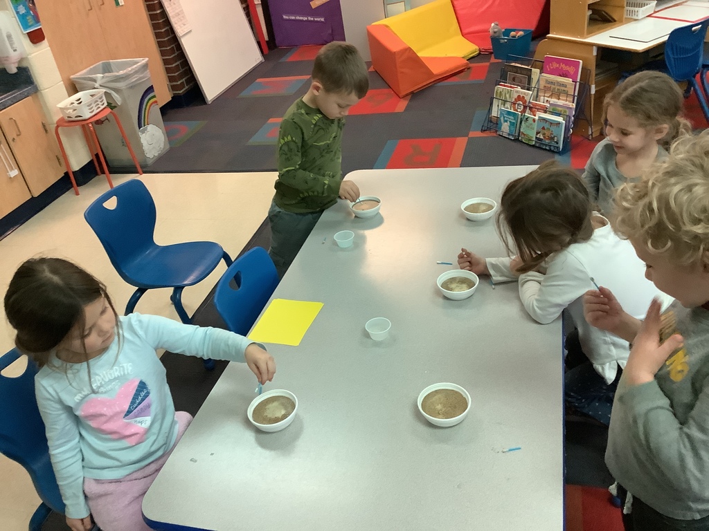 Kids are sitting at a table.  Each has a bowl with pepper on top of water.  They have a Q-tip that they have or are dipping into the bowl.