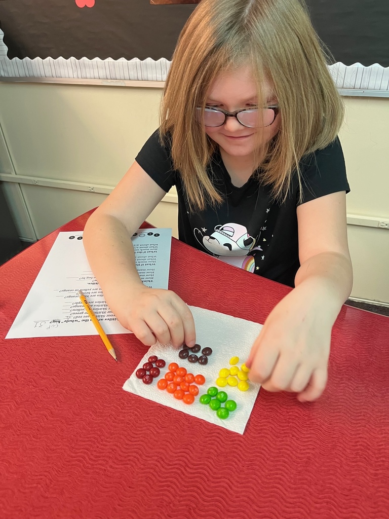 female student in black shirt working on math problem with Skittles separated into piles based on color.