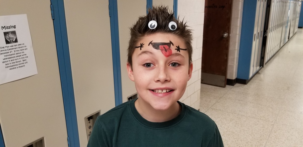 Boy in black shirt with brown hair spiked up, 2 toy eyes stuck in it and a mouth and 2 hands painted across forehead.