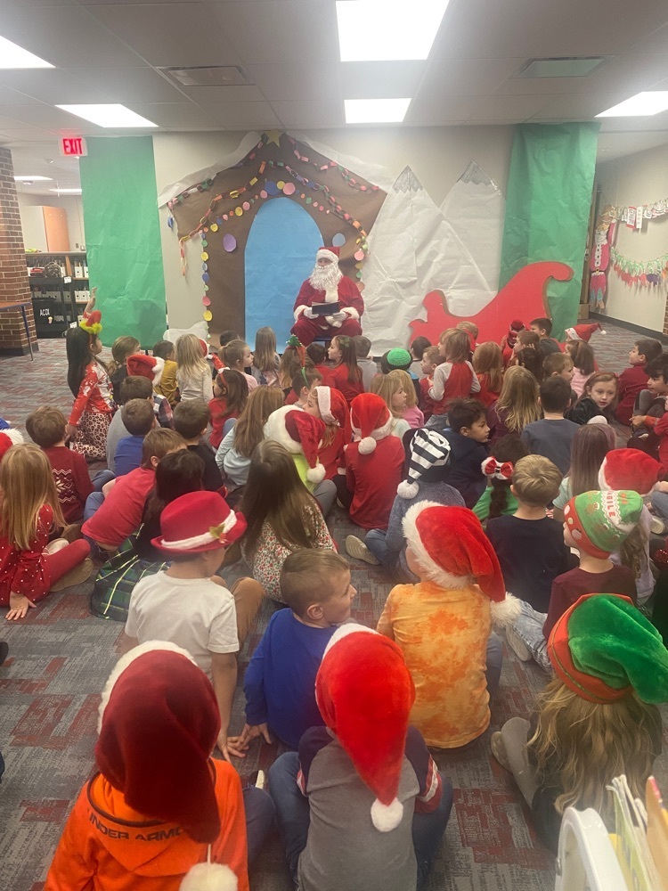 a group of kindergarten students sitting on a carpet and listening to Santa reading a story 