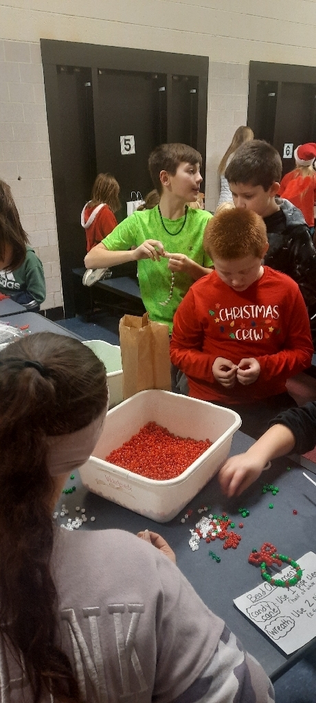 2 students wearing red and green standing behind a white bin full of red beads.