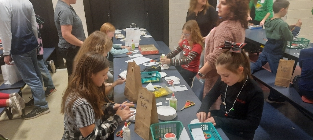 5 female students sitting at long blue table with craft supplies in front of them.