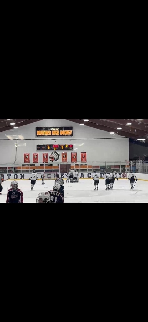hockey players on ice with scoreboard and flags in background