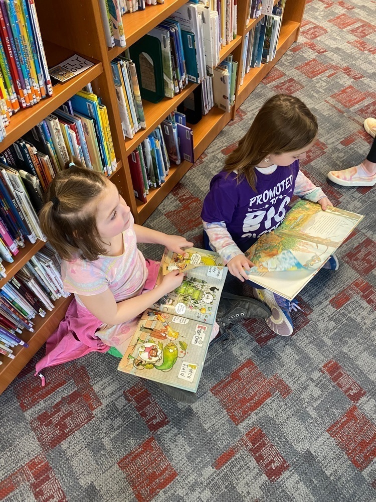 Two students sitting cross legged on the floor with open books on their laps