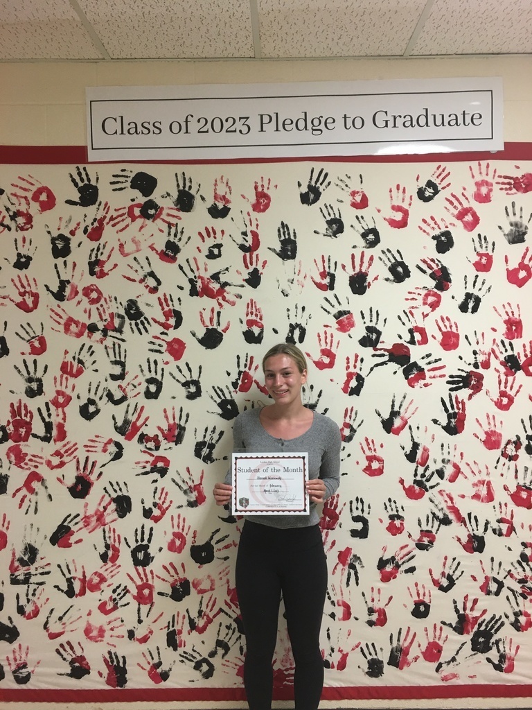 Girl with certificate standing in front of a wall with black and red handprints