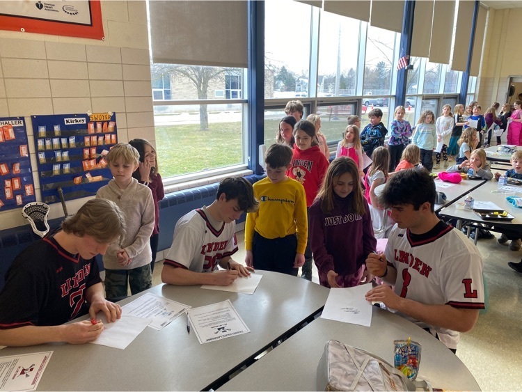 Picture of high school lacrosse players signing autographs at the lunch table at Hyatt Elementary 