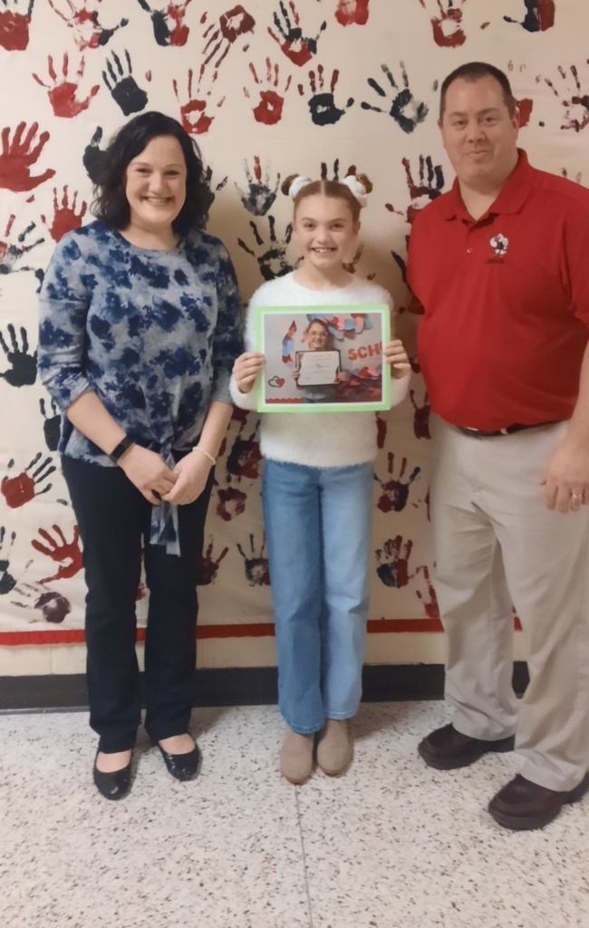 Teacher, student, and principal standing in front of a wall with red and black handprints on it.