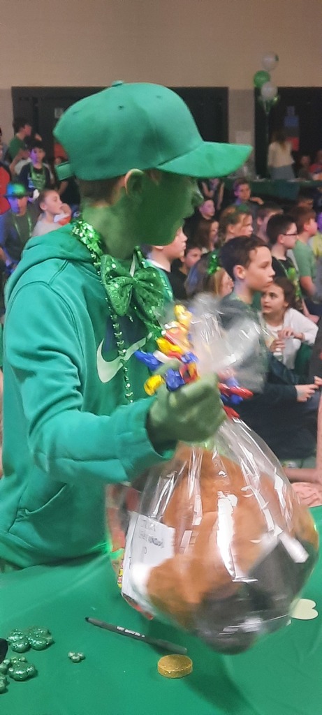 An elementary student wearing green pants, green sweater, green hat and face painted green.