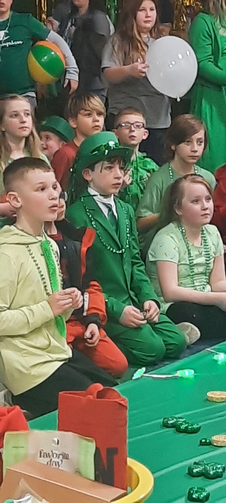 several students looking at the same person. Middle student is wearing a green suit with a white dress shirt, sparkly green tie and green top hat.