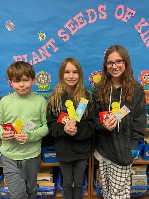 3 students holding a candy bar and 2 bookmarks.