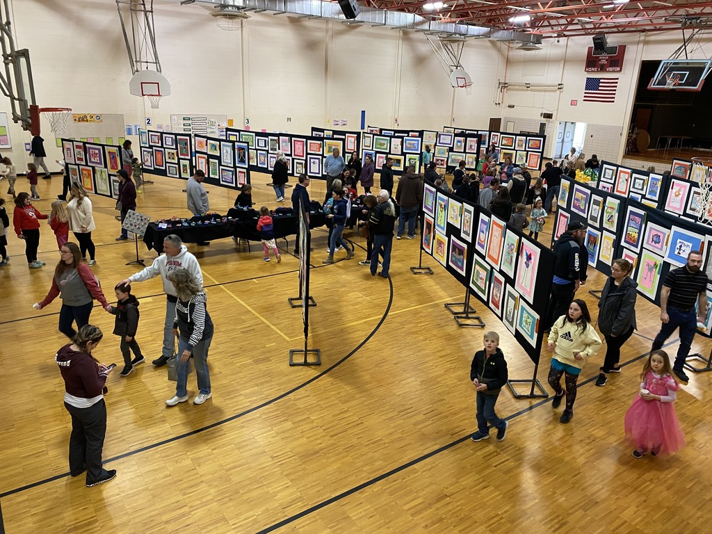 Multiple families walking around a gymnasium looking at pictures of student art.