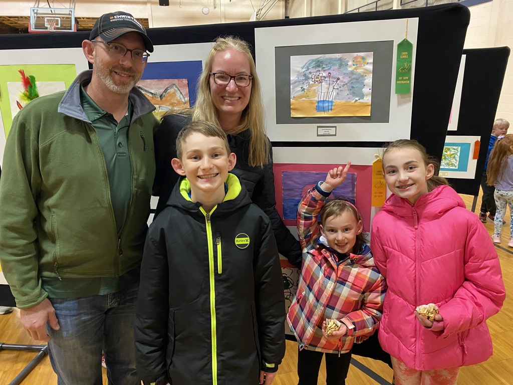 A family of five smiling in front of their child's artwork.